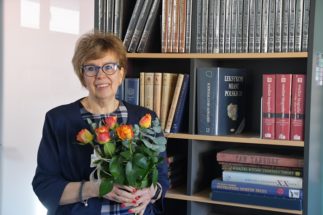 Kobieta w okularach z bukietem kwiatów w ręku. Z tyłu półki z książkami.