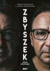 okładka książki, pół twarzy mężczyzny w okularach w odbiciu lustrzanym, u góry napis: Zbigniew Zamachowski w rozmowie z Beatą Nowicką, po środku z góry na dół dalszy ciąg napisu: Zbyszek : przez przypadki, Znak